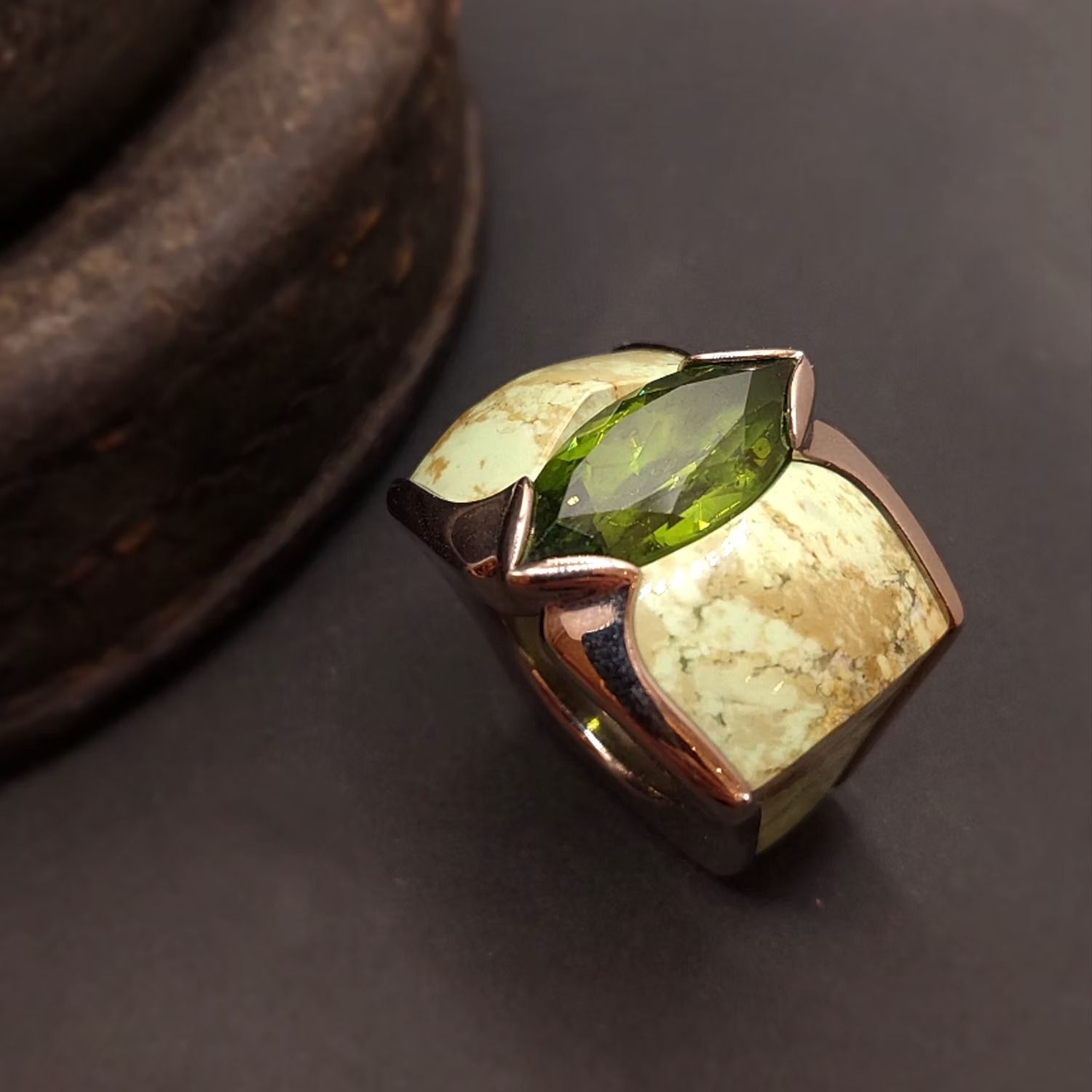 Nahaufnahme eines silbernen Rings mit einem grünen und einem cremefarbenen Edelstein auf dunklem Untergrund