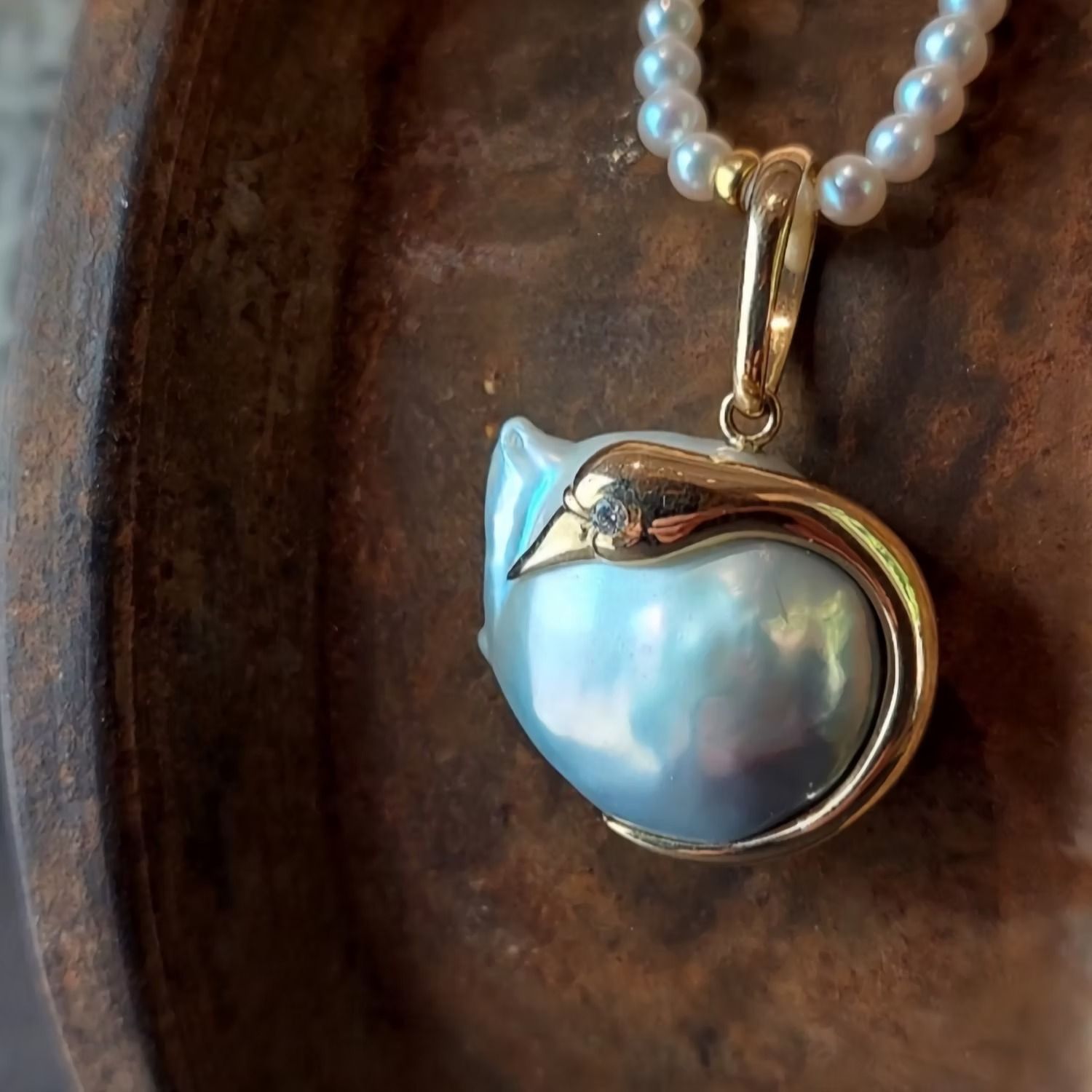 Halskette mit Anhänger, bestehend aus einer großen, birnenförmigen Perle in Goldfassung und einem kleinen Diamanten an einer Perlenkette, die auf einer Holzoberfläche ruht.