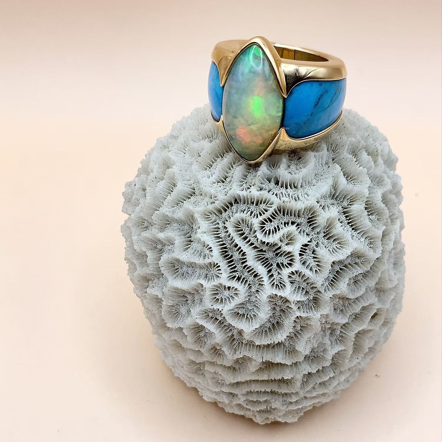 Goldring mit Opal- und Türkissteinen auf weißer Koralle.