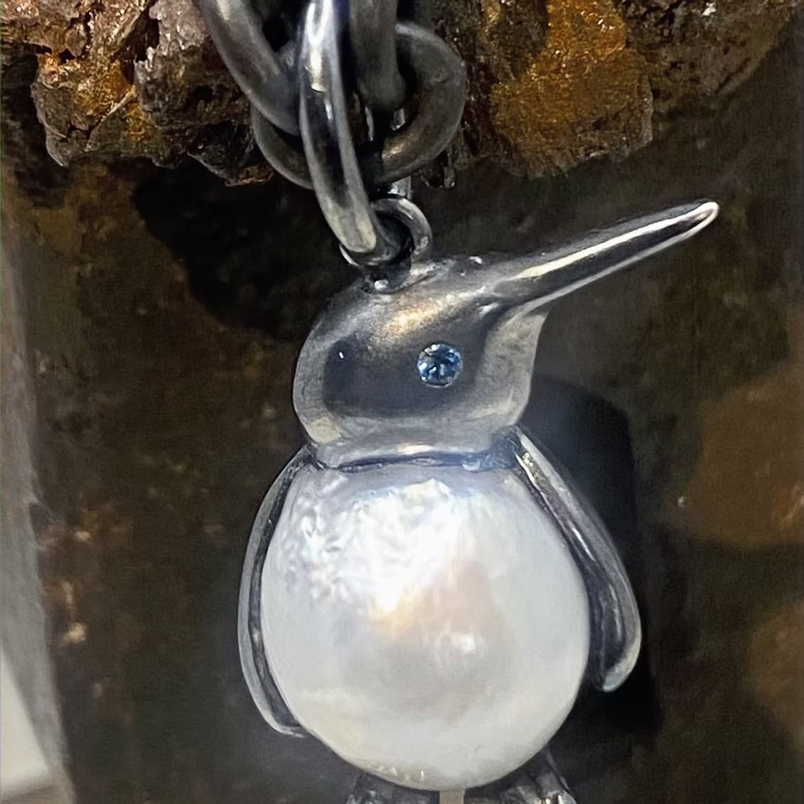 Silberner Pinguinanhänger mit Perlenkörper und blauem Edelsteinauge an einer Kette.