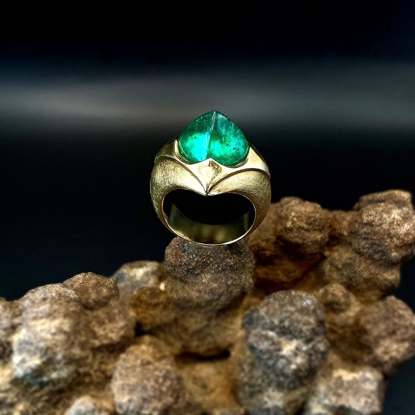 Goldring mit grünem Edelstein, der auf Felsen vor dunklem Hintergrund ruht