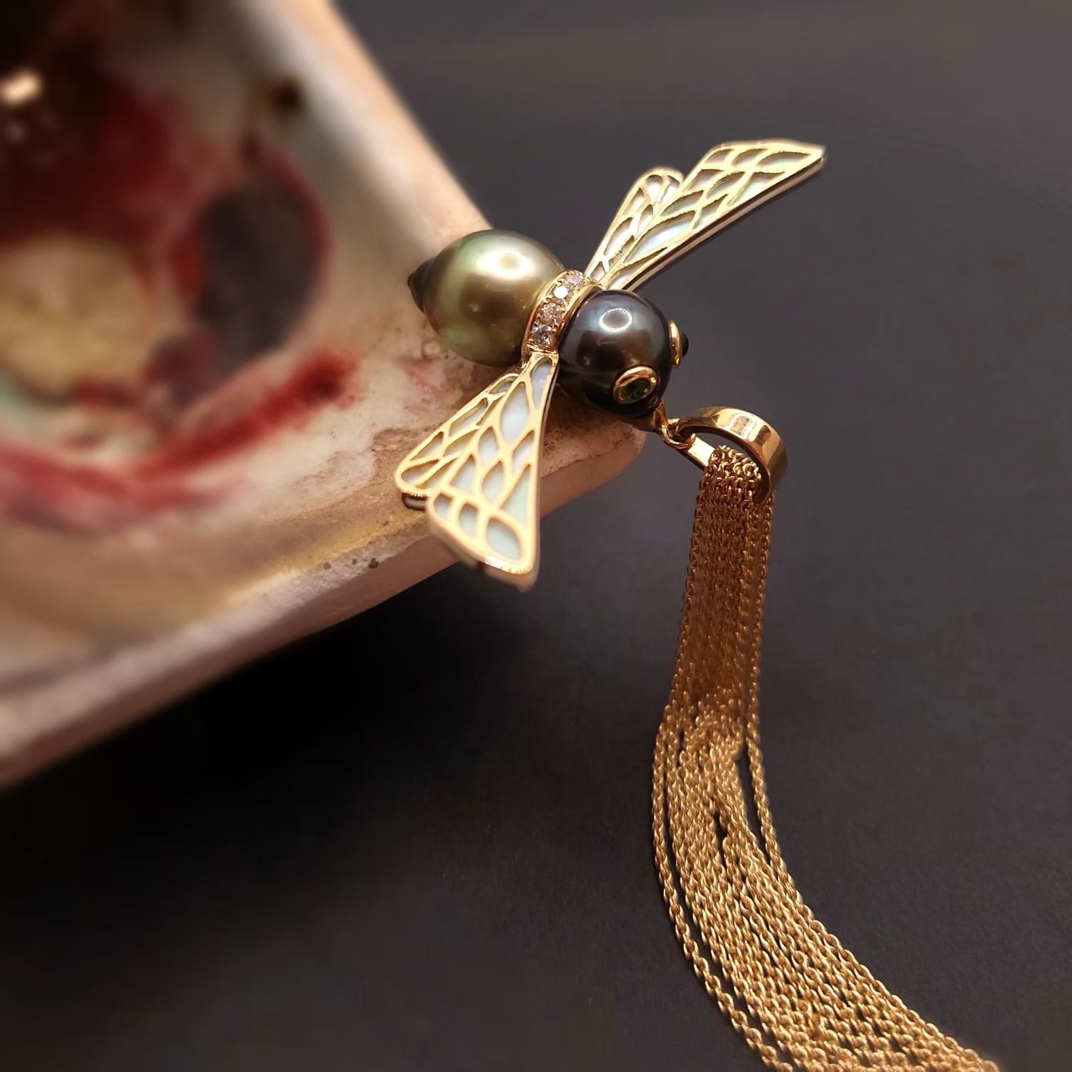 Goldener Bienenanhänger mit Perlenkörper, weißen Emailleflügeln und goldener Quaste.