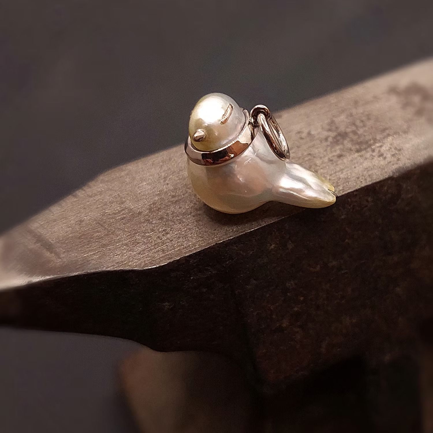 Ein Vogelanhänger aus Perlen auf einem Amboss; silberne Akzente, auf Metall befestigt.