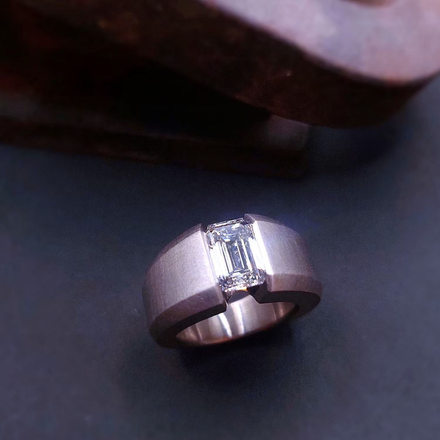 Silberner Ring mit einem rechteckigen Diamanten, eingefasst in dunkles Material.