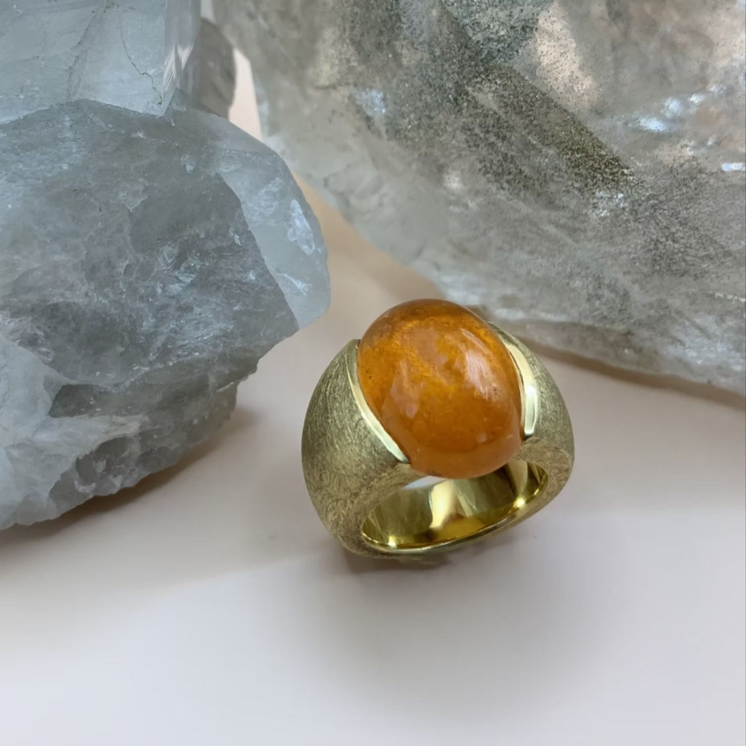 Goldring mit einem großen, ovalen, orangefarbenen Edelstein vor mattiertem Hintergrund.