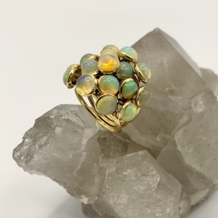Goldring mit mehreren Opal-Cabochons, ruhend auf einem rohen Quarzkristall.