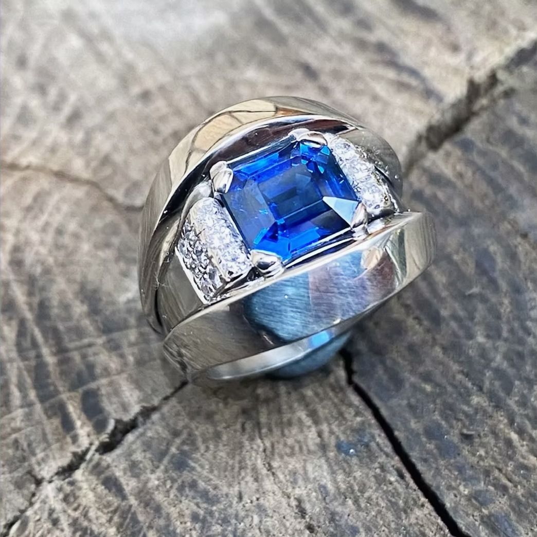 Silberner Ring mit großem blauen Edelstein und kleinen Diamanten, gefasst in Holz.