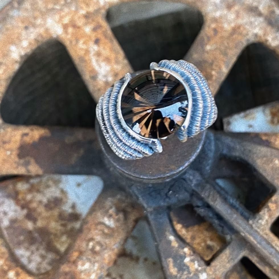 Ring mit dunklem Edelstein und wellenförmiger Fassung auf einem rostigen Metallrad.