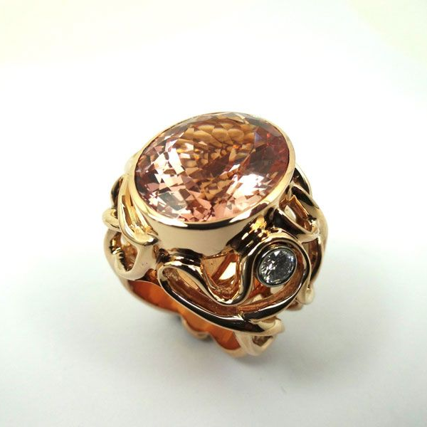 Verzierter Goldring mit einem großen ovalen rosa Edelstein auf weißem Grund