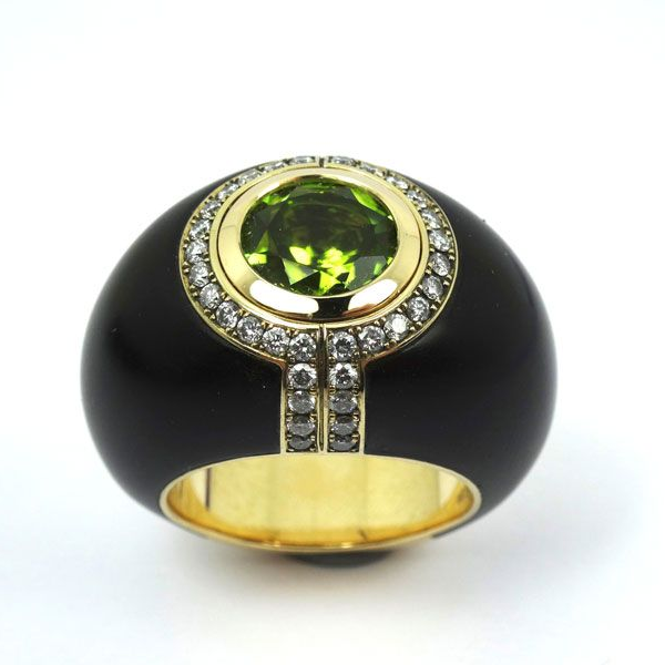 Schwarzer und goldener Ring mit einem großen grünen Edelstein und kleinen klaren Steinen