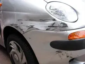 Hopeisen auton etuosa, jossa naarmuja ja lommoja puskurissa ja lokasuojassa