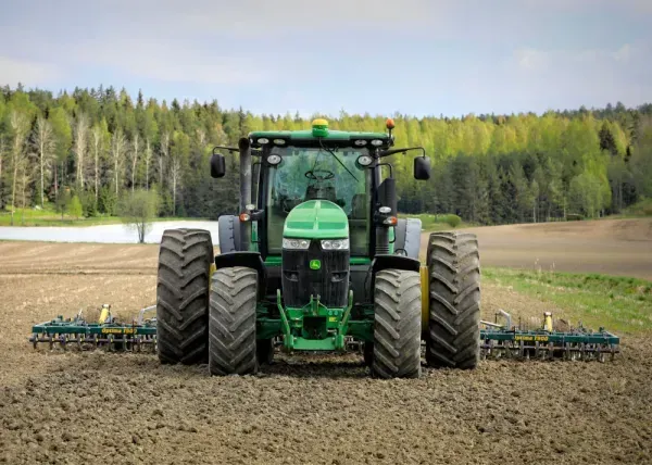 Vihreä traktori kylvää satoa pellolla, taustalla metsä