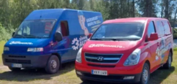 Kaksi pakettiautoa, yksi sininen ja yksi punainen, pysäköitynä nurmikolle ulkona.