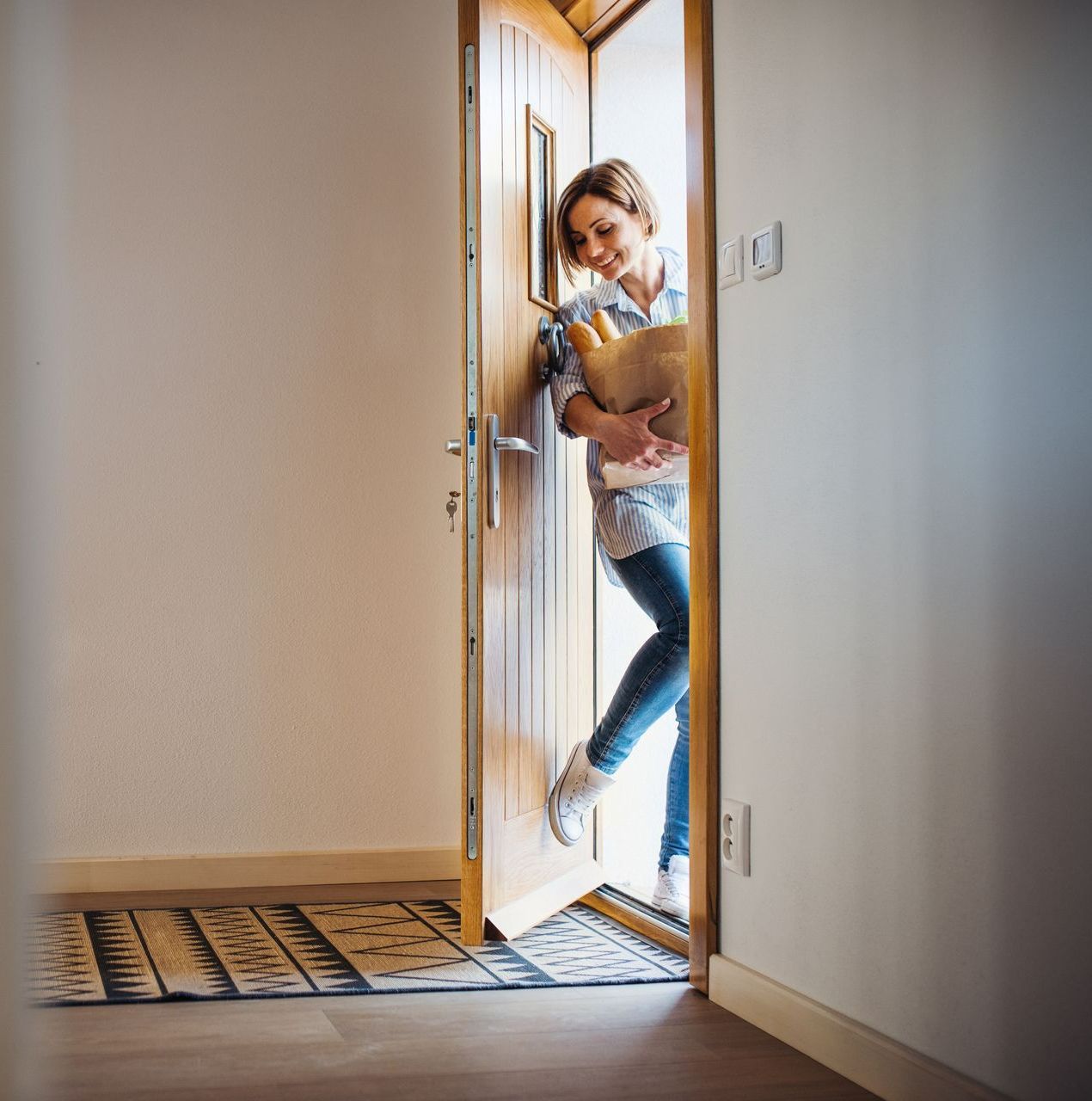 Un femme portant des courses rentre par une porte d'entrée