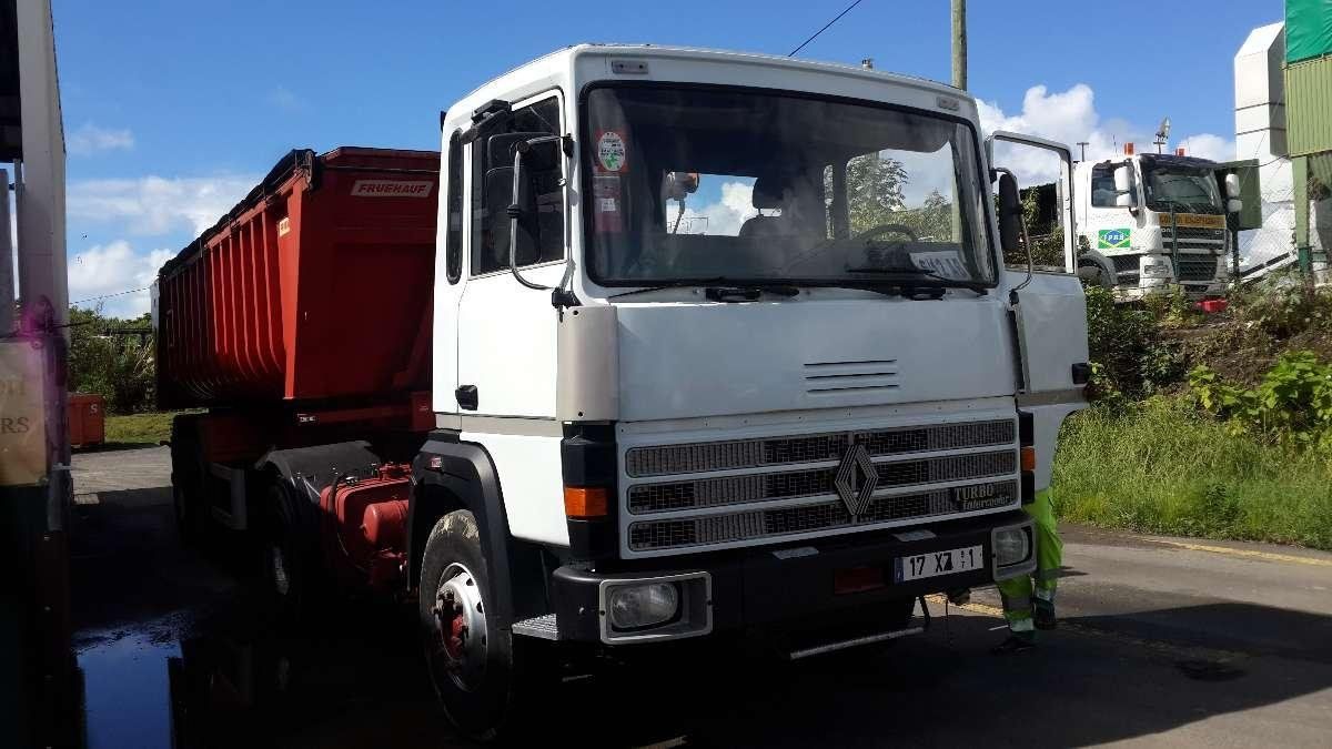 Un camion-benne blanc est arrêté un conteneur rouge à l'arrière, sous un ciel d'un bleu éclatant.