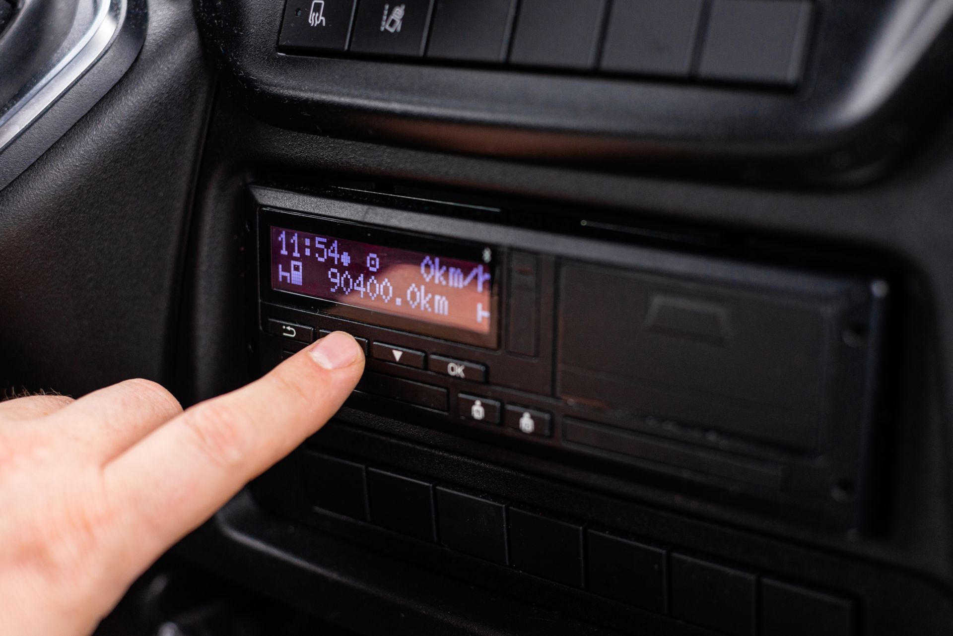 Appui d'un doigt sur un bouton d'un autoradio affichant un petit écran avec des chiffres en violet.