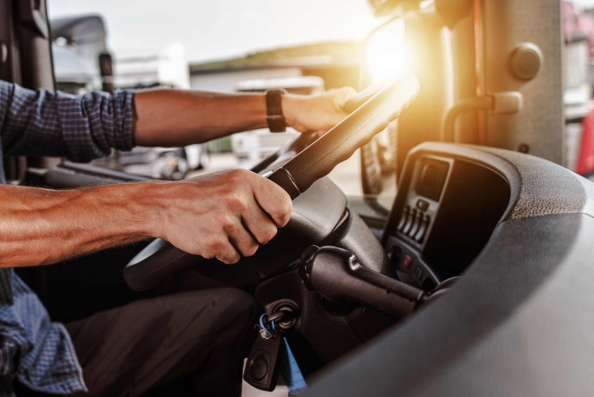 Un conducteur tient le volant dans la cabine de son camion au coucher du soleil, le tableau de bord est visible.