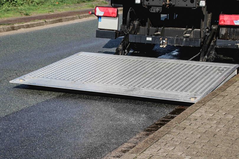 Camion de chantier déposant une rampe métallique sur de l'asphalte frais sur une route