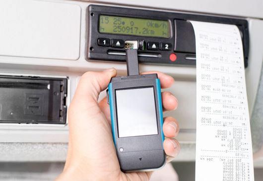 Une main tenant un appareil portable à écran vierge à côté d'une imprimante et d'un rouleau de reçus imprimés.
