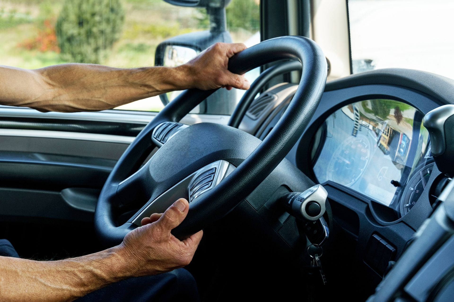 Les mains du conducteur sur le volant à l'intérieur d'un camion, la route reflète dans le tableau de bord.