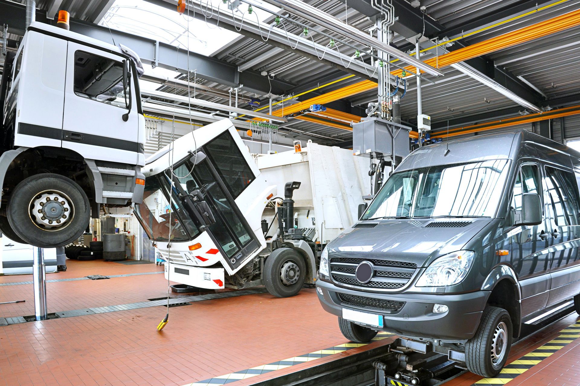 Des cabines de camion dans un atelier, l'une inclinée sur un pont élévateur et une camionnette grise à droite.