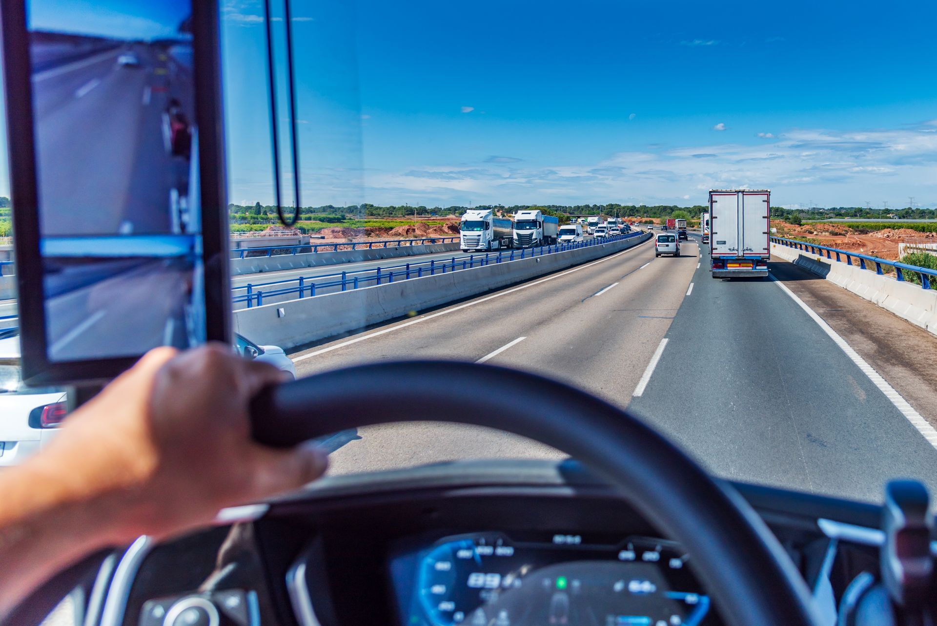 Vue du conducteur sur une autoroute, main sur le volant, suivant un camion blanc sous un ciel bleu dégagé
