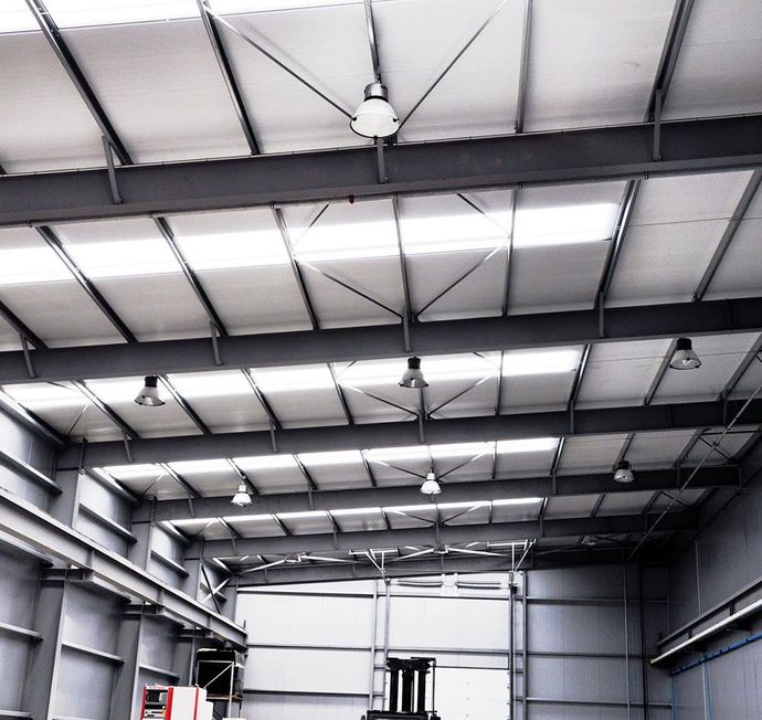 Intérieur d'un grand entrepôt industriel avec un haut plafond métallique et des puits de lumière.