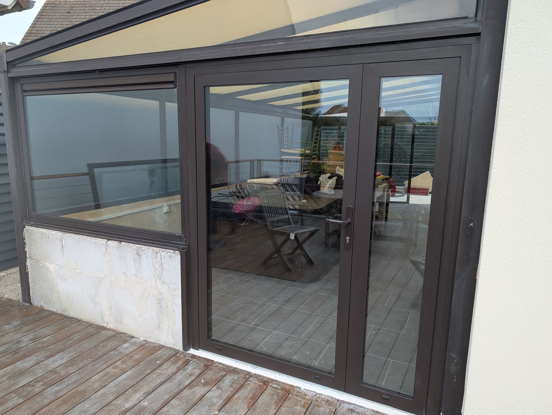 Portes et fenêtres vitrées à cadre brun d'une véranda, reflétant une table à manger et un espace extérieur.