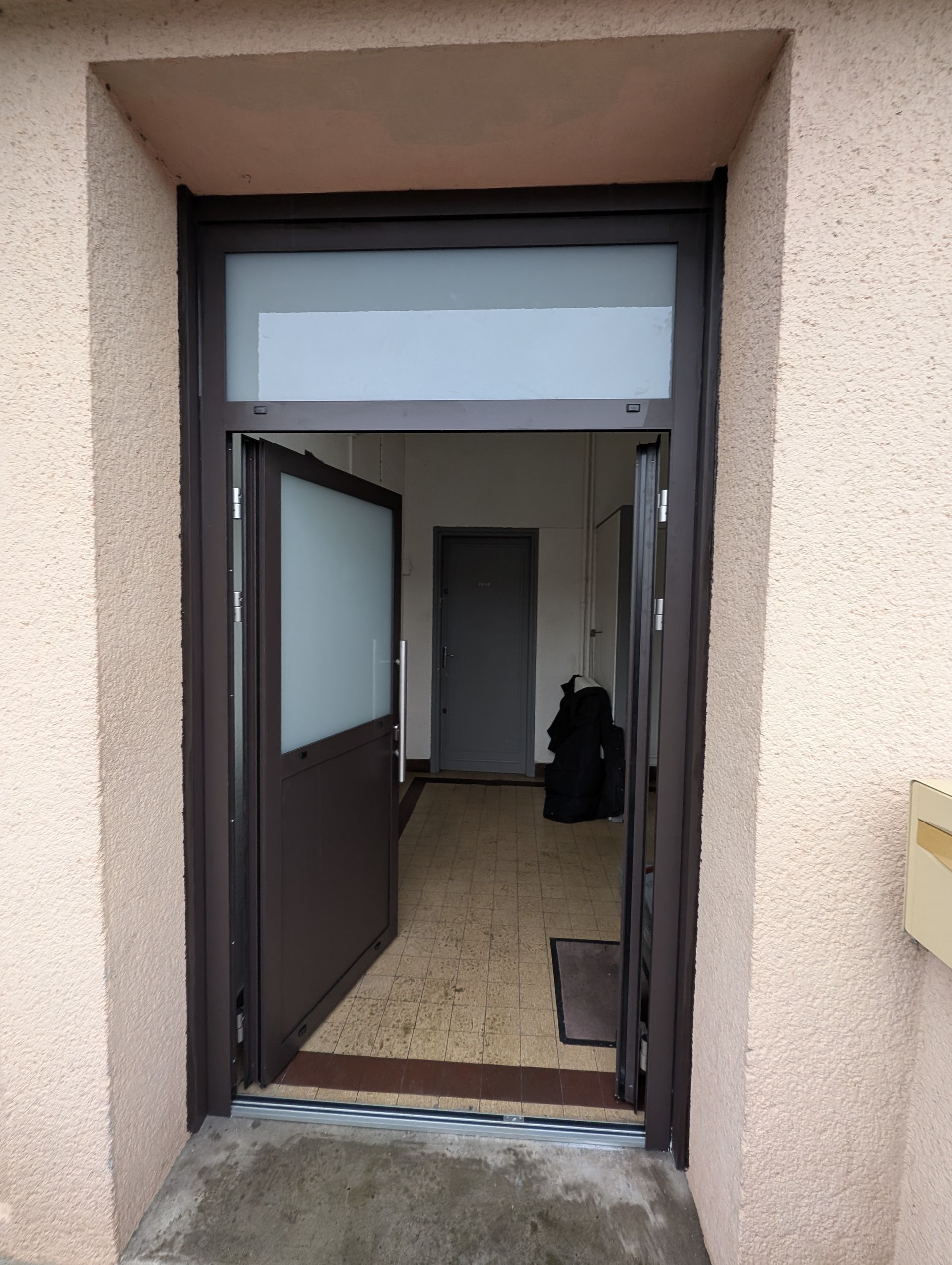 Porte à cadre brun avec vantaux partiellement ouverts, révélant un couloir intérieur.