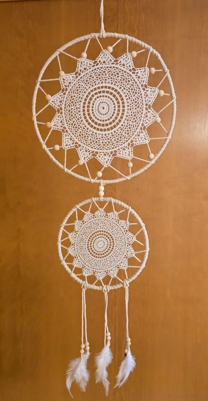 An einer Holzwand hängen zwei weiße Traumfänger.