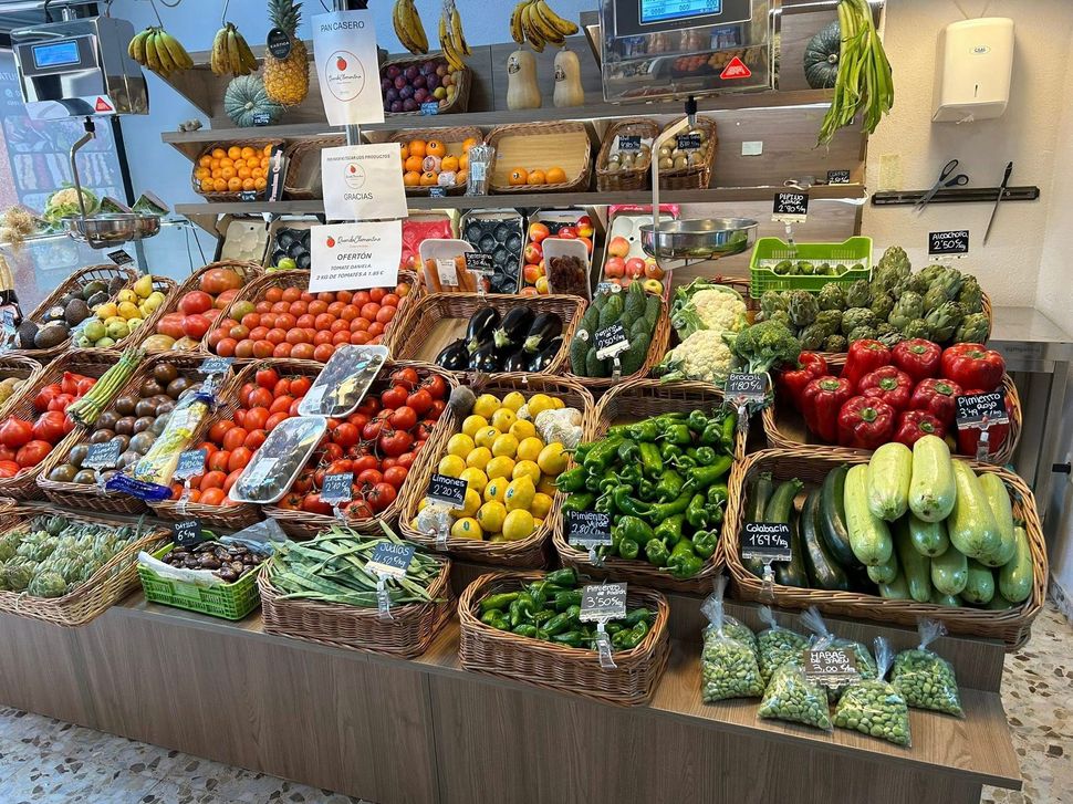 Exhibición de frutas y verduras frescas variadas en cestas y recipientes de mimbre en un puesto de mercado.