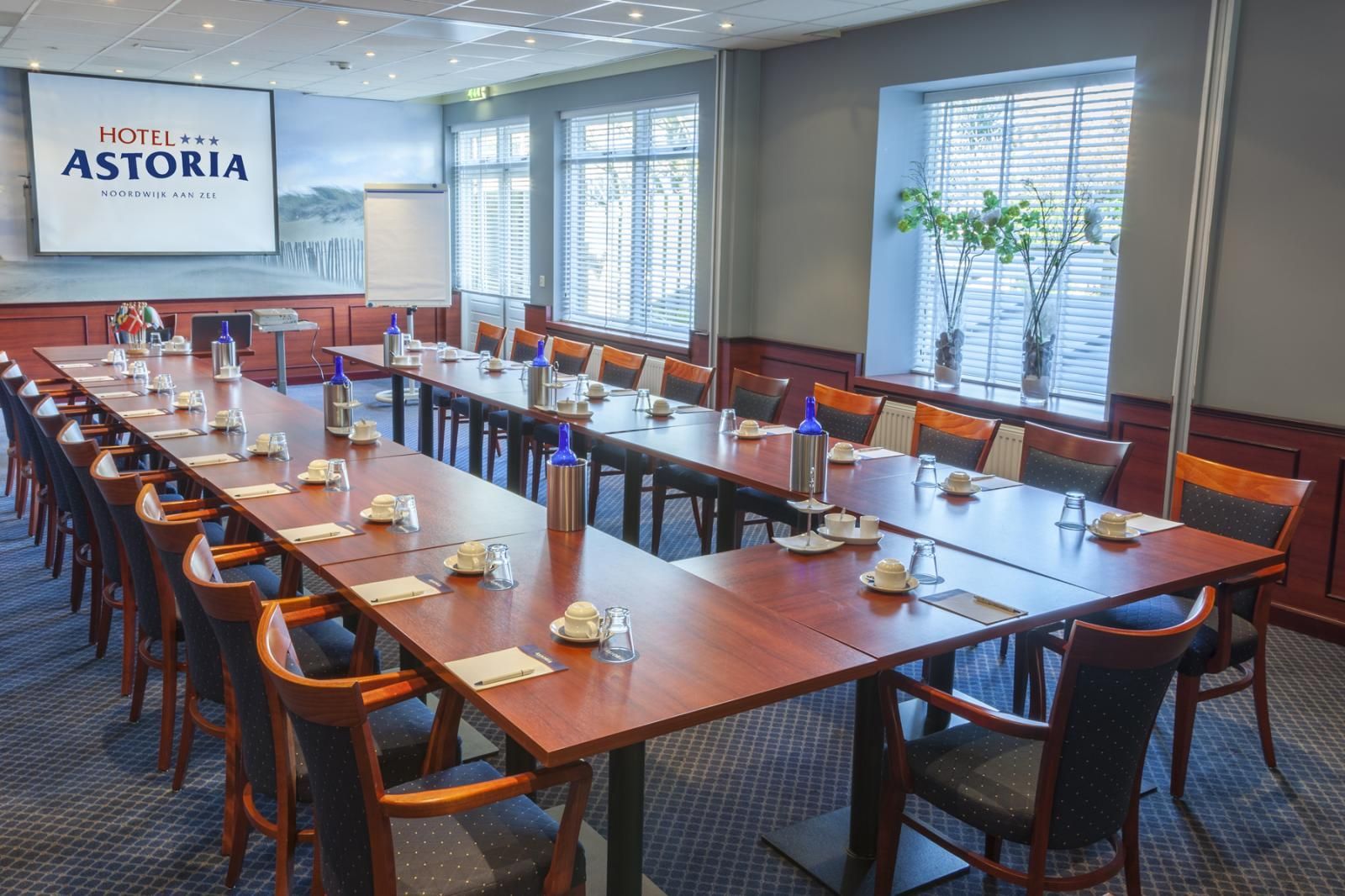 Een grote conferentieruimte met tafels en stoelen, klaar voor een vergadering.