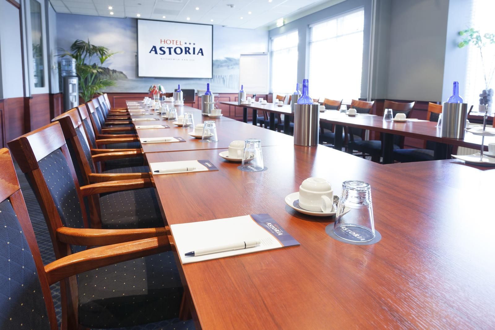 Een vergaderruimte met een lange tafel en stoelen, klaar voor een vergadering.