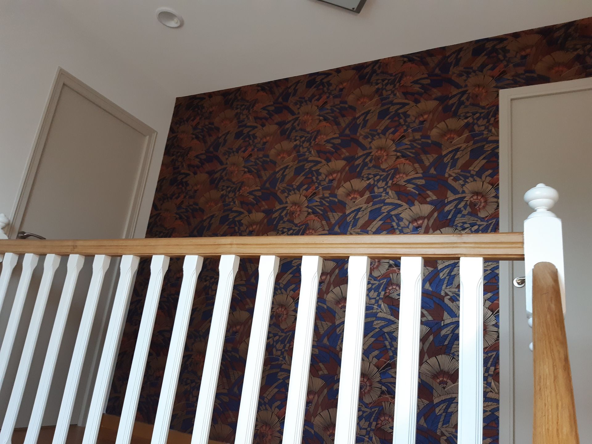 Hall d'escalier avec garde-corps en bois et peint en blanc avec papier peint floral rouge et bleu en fond
