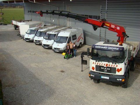 Ein weißer MAN-Lkw mit rotem Kran parkt neben einer Reihe weißer Service-Lieferwagen vor einem Lagerhaus.