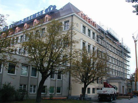 Ein großes, hellfarbiges Gebäude mit einem mehrgiebeligen Dach und einem Gerüst an der Seite, von der Straße aus gesehen.