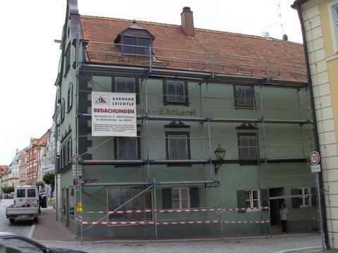 Ein hellgrünes Gebäude, das derzeit renoviert wird und an dessen Fassade ein Gerüst angebracht ist, befindet sich an einer Straßenecke in der Stadt.