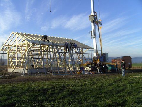 Arbeiter errichten an einem sonnigen Tag mit Hilfe eines Krans eine Holzrahmenkonstruktion auf einem Feld.