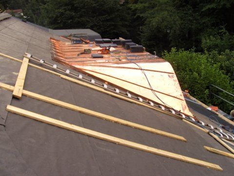 Ein im Bau befindliches, geneigtes Wohnhausdach mit Holzlatten, freiliegender Sperrholzschalung und schwarzer Dachunterspannbahn.