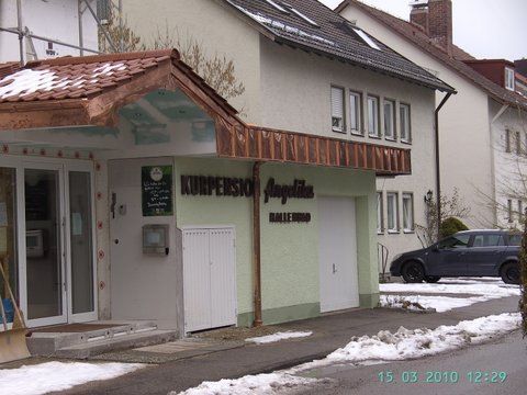 Ein hellgrünes Gebäude mit der Aufschrift „Pension Angelika“ und einem kupferverzierten Dach, teilweise mit Schnee bedeckt, in der Nähe einer Straße.