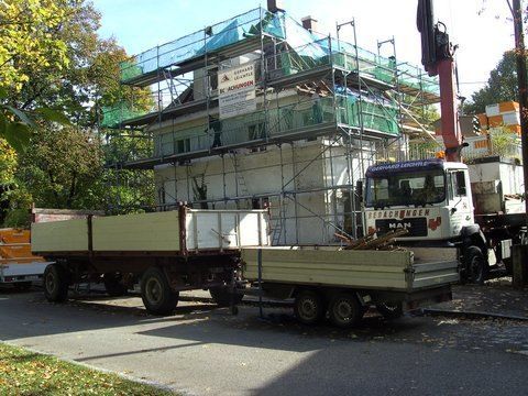 Ein Haus, das wegen Renovierungsarbeiten mit einem Gerüst versehen ist, davor steht ein Baukranwagen.