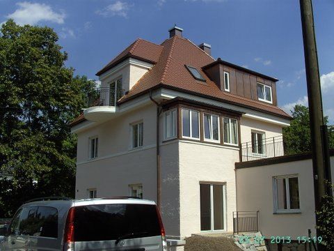 Ein zweistöckiges Stuckhaus mit Ziegeldach, Erkerfenstern, einem Balkon und einem im Vordergrund geparkten weißen Lieferwagen.