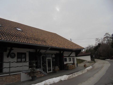 Ein weißes Bauernhaus mit braunem Ziegeldach und Holzbalken steht an einer Straße, auf der ein Fleck Schnee liegt.