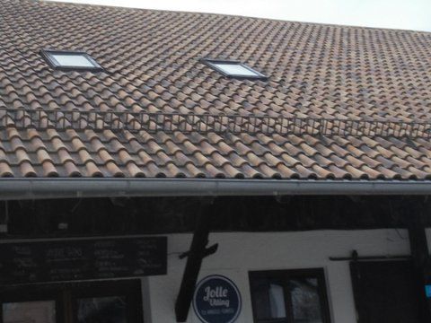 Ein Ziegeldach mit zwei Oberlichtern über einem weißen Gebäude mit einem runden Jolle-Schild in der Nähe des Eingangs.