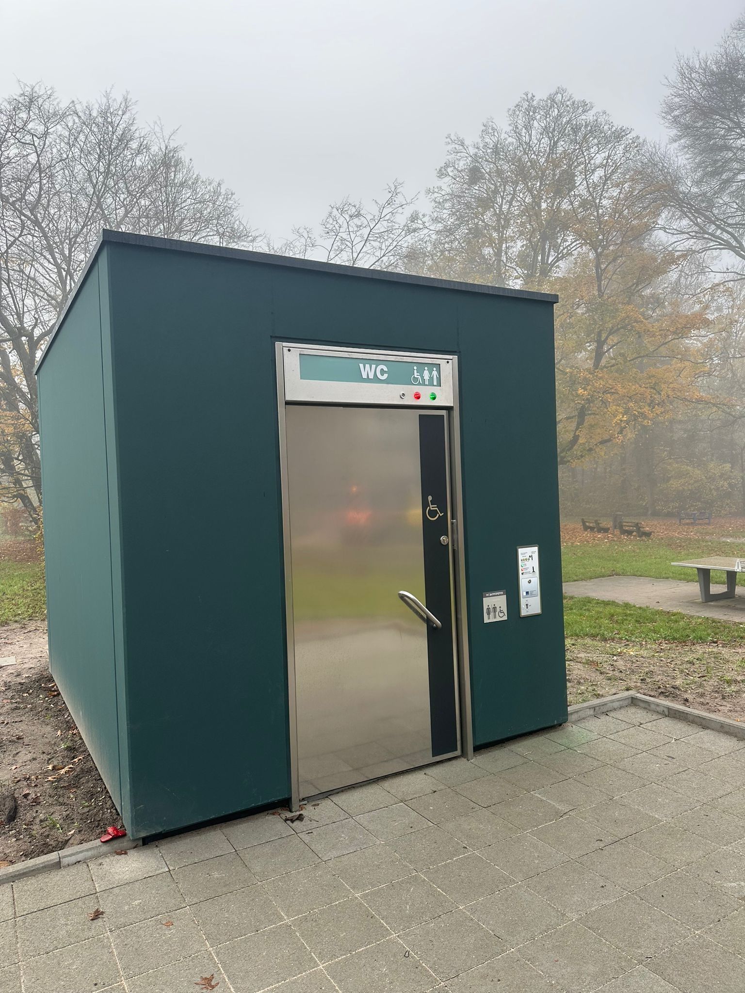 Außenansicht einer öffentlichen Toilettenkabine mit Edelstahltür im Park.