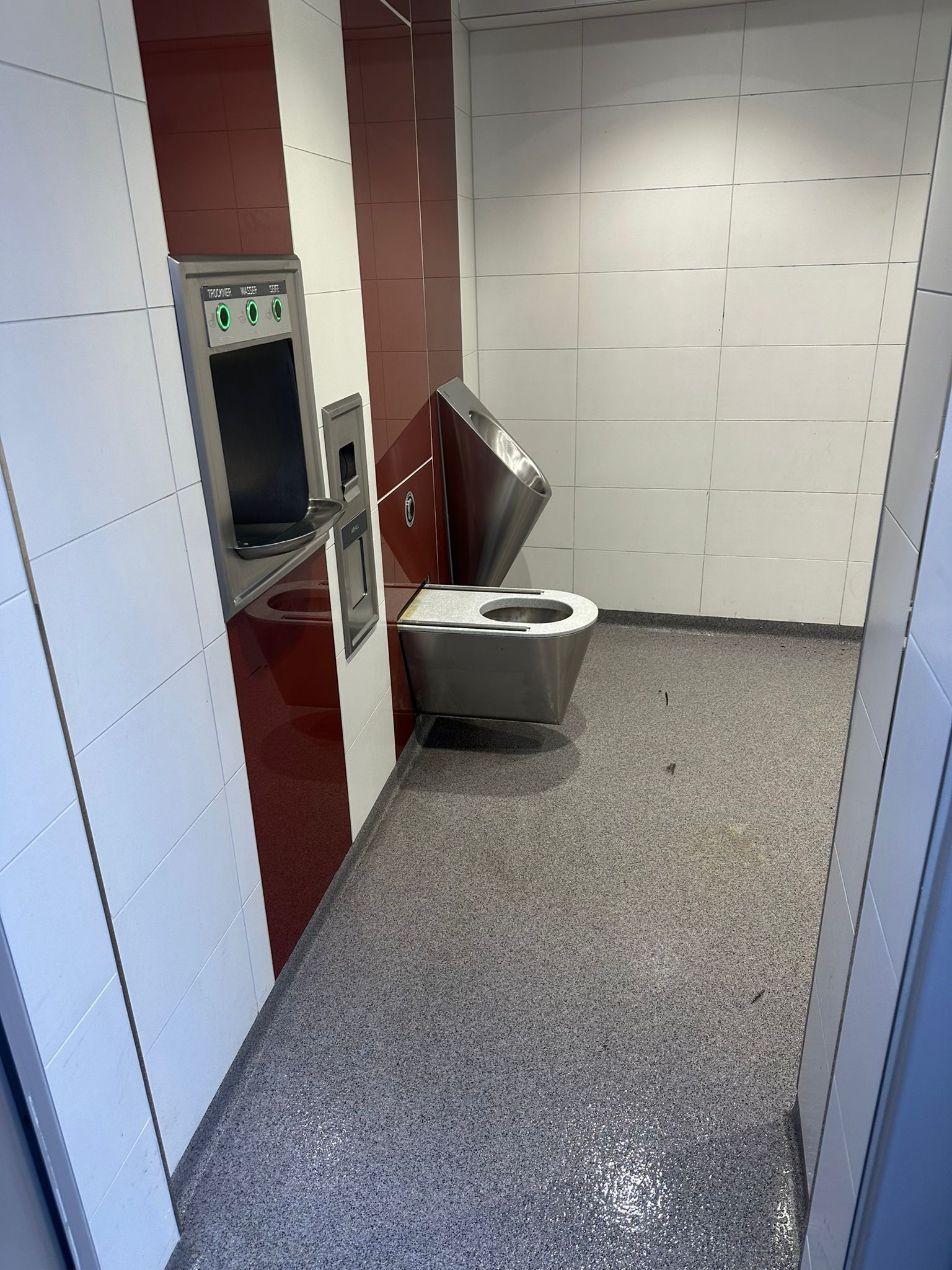 Innenraum einer Toilettenkabine mit modernem Edelstahl-WC und Wandpaneelen.