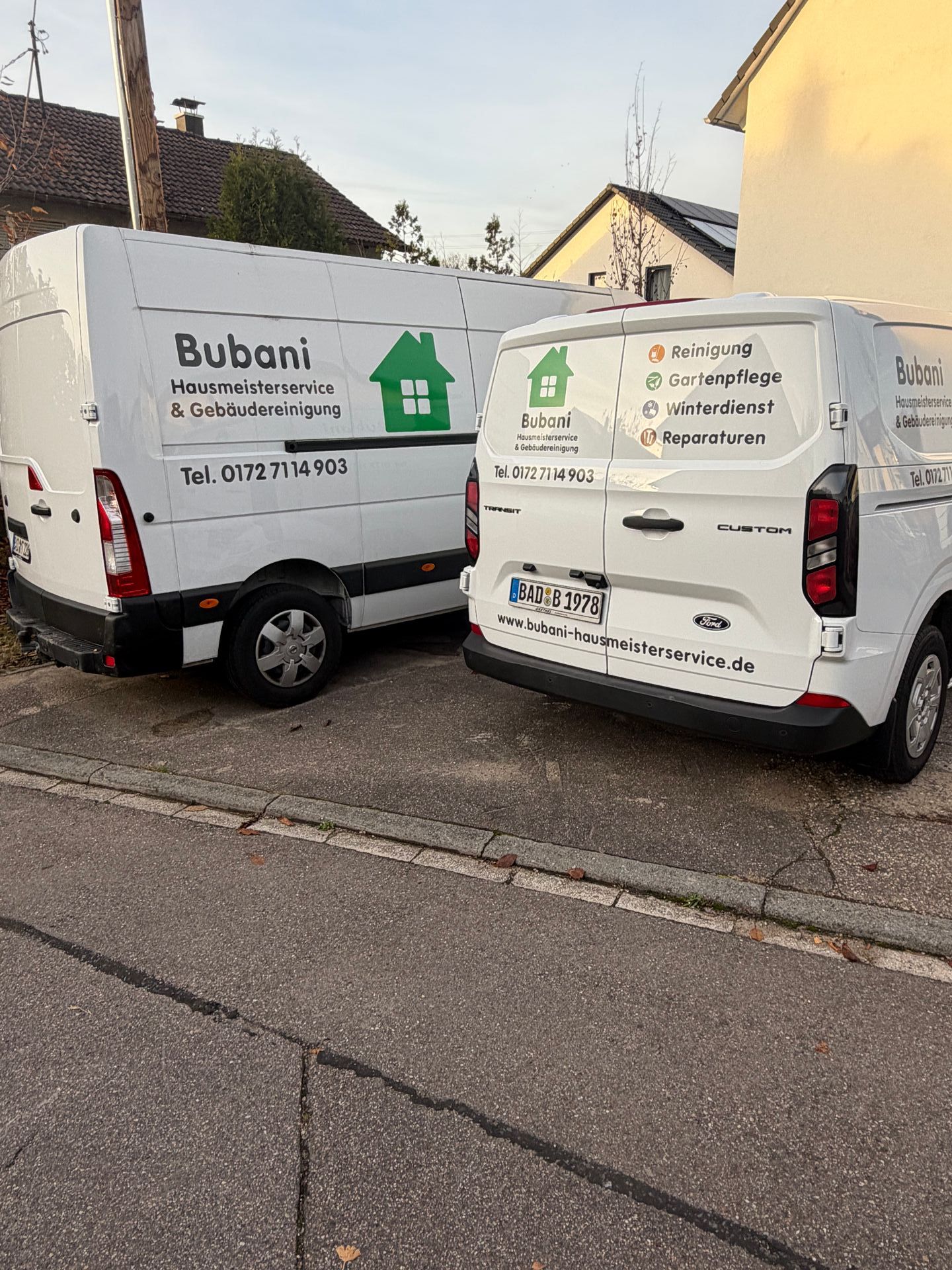 Zwei Servicefahrzeuge eines Hausmeisterservice mit Firmenbeschriftung auf einem Parkplatz.