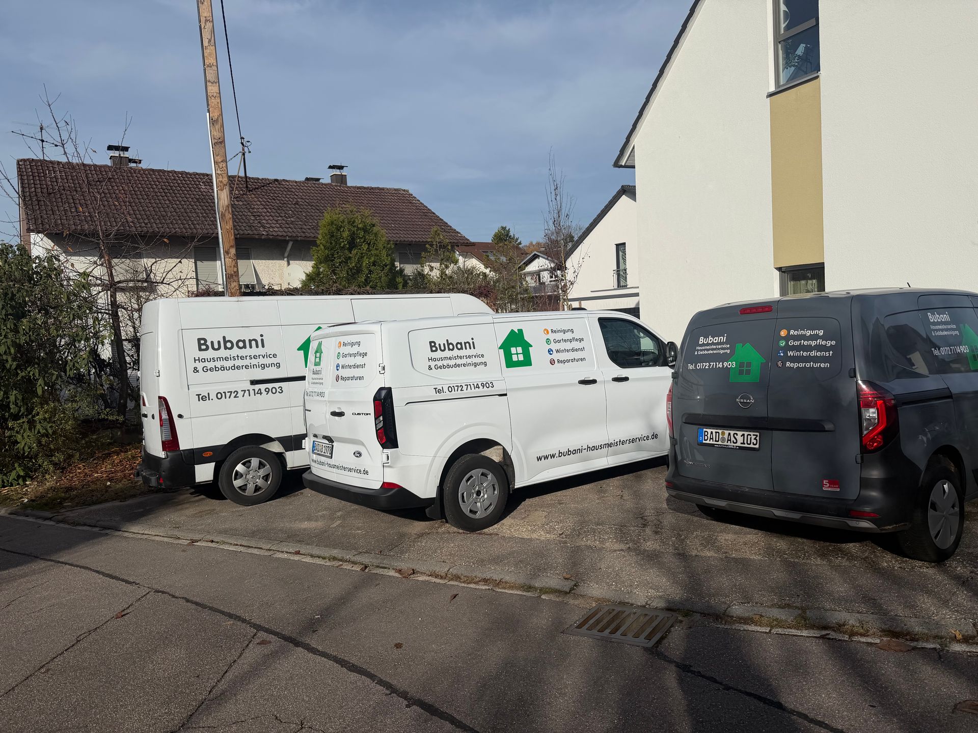 Mehrere Servicefahrzeuge eines Hausmeisterservice auf einem Parkplatz vor Wohnhäusern.