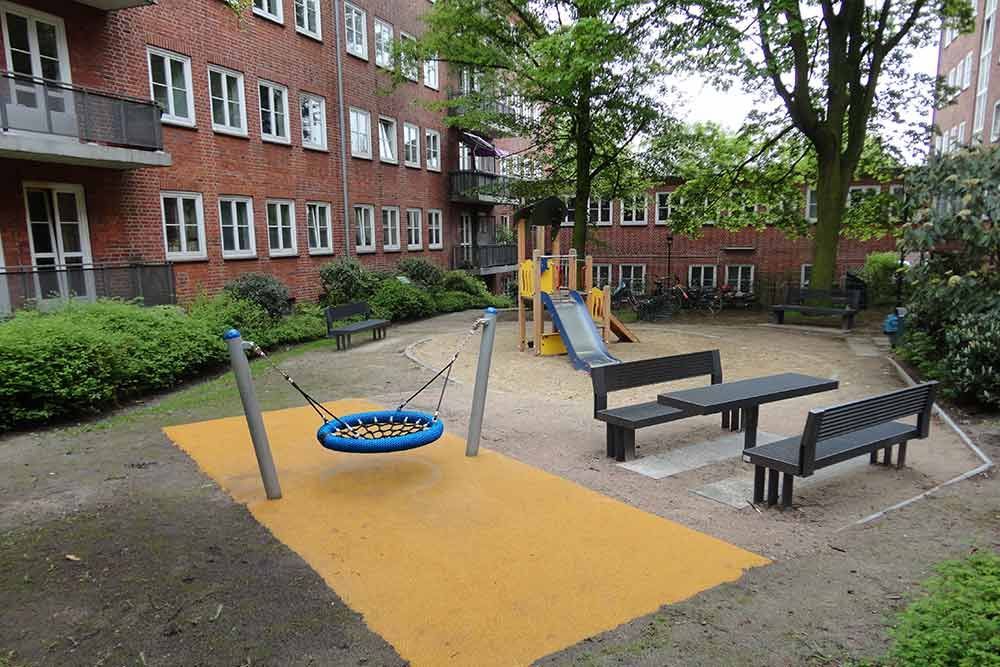 Ein Spielplatz mit Schaukel und Bänken vor einem Backsteingebäude