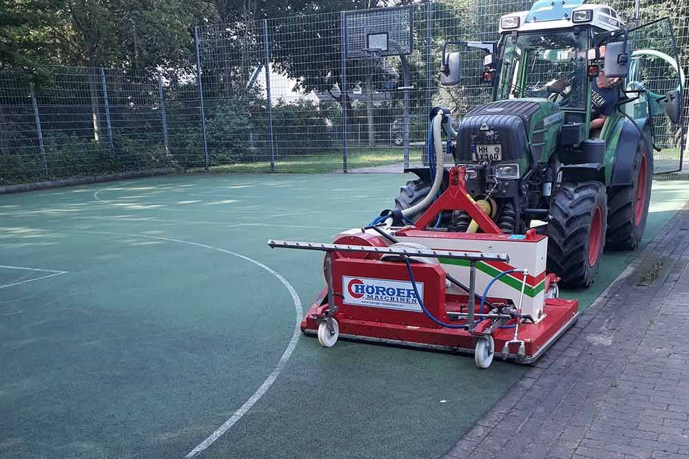Ein Traktor reinigt mit einer Maschine einen Tennisplatz.